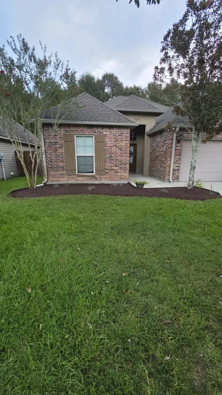 Finished Denham Springs front bed with fresh black mulch, steel edging, and ornamental grasses along a brick house.