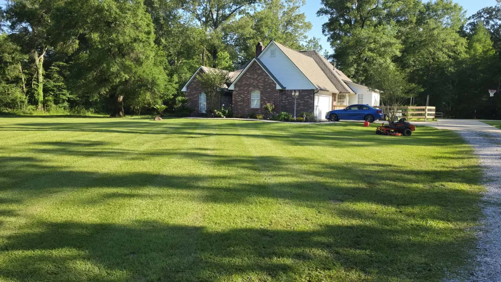 Freshly striped green residential lawn with an orange Bad Boy Magnum zero-turn parked by the driveway.